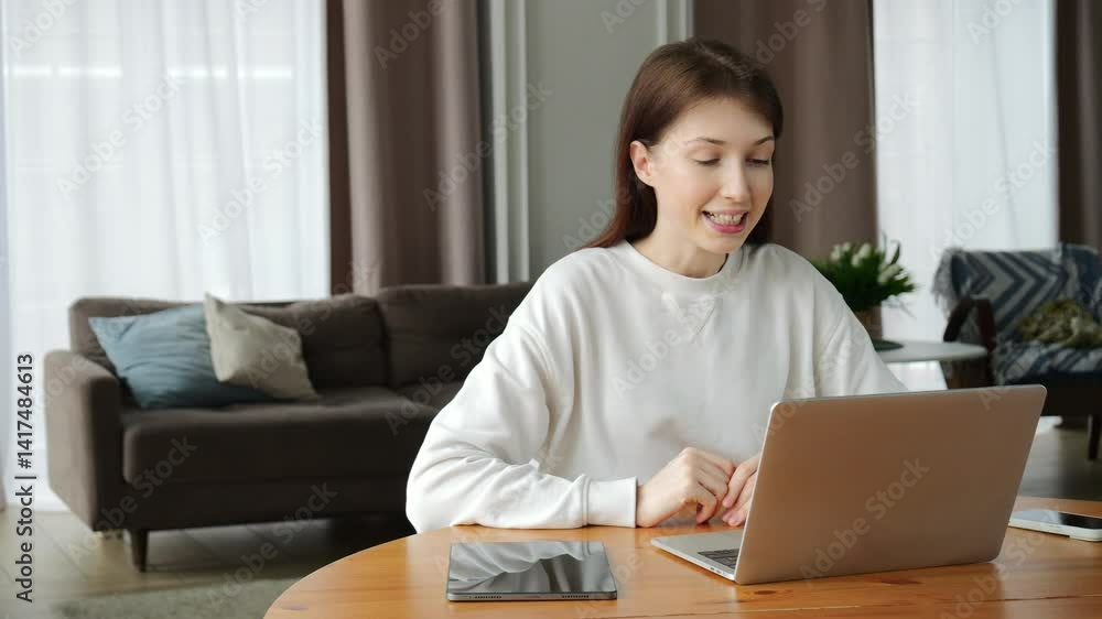 Woman cheerfully greets participants with a wave during a friendly online chat at her desk. Woman cheerfully greets participants with a wave during a friendly online chat at her desk.