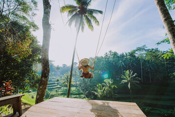 Beautiful girl visiting the Bali rice fields in tegalalang, ubud. Using a swing over the jungle. Concept about people, wanderlust traveling and tourism lifestyle