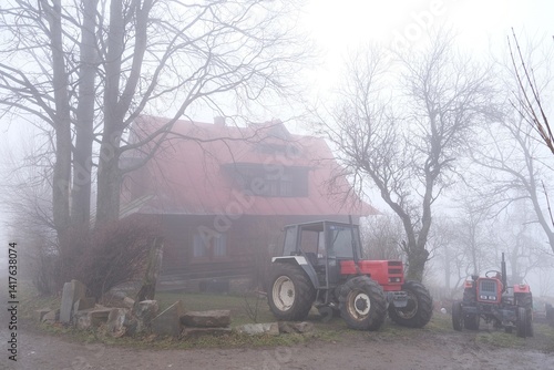 Obraz na płótnie Very misty scenery tractor standing next to farm building in village. w salonie