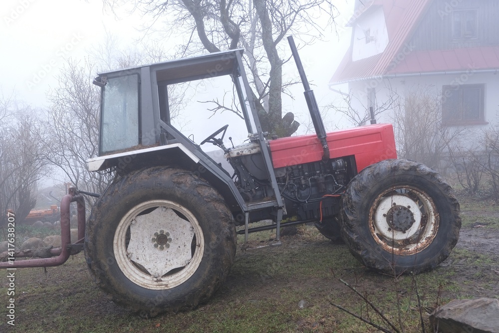 Very misty scenery tractor standing next to building in village.