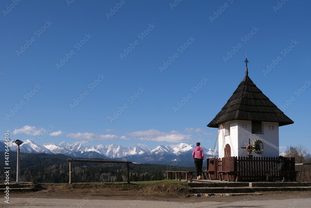 Viewpoint of High Tatras and Bialskie Tatras on Pass over Lapszanka with old white chapel and silhouette of woman in pink jacket.