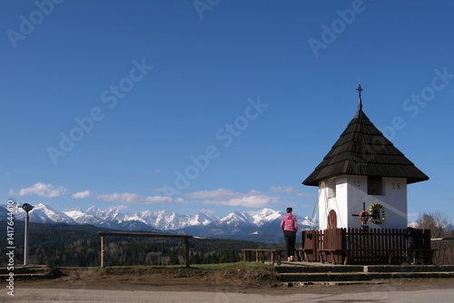 Obraz na płótnie Viewpoint of High Tatras and Bialskie Tatras on Pass over Lapszanka with old white chapel and silhouette of woman in pink jacket. w salonie