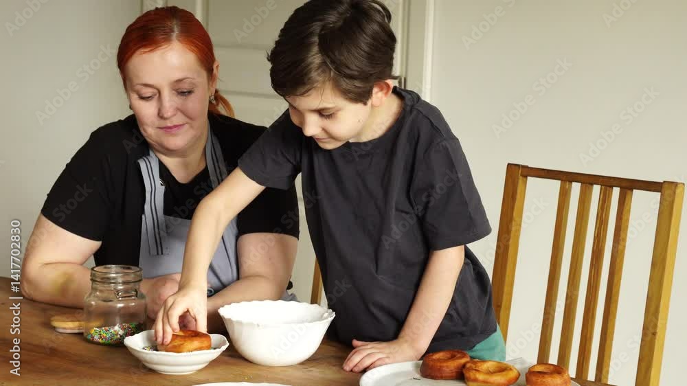 Mother with son apply glaze and sprinkle to donuts Mother with son apply glaze and sprinkle to donuts