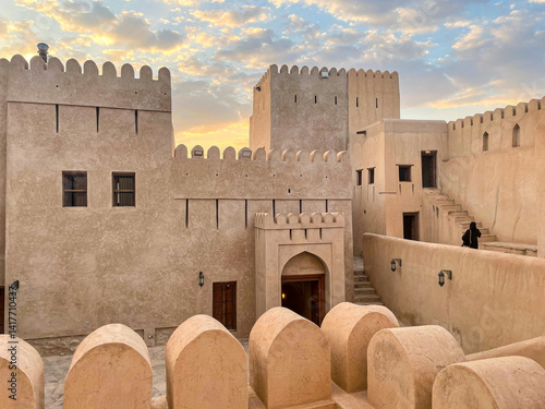 Nizwa Fort in Oman at sunset - Ancient mud brick fortress with crenellated walls, watch towers and courtyard under dramatic cloudy sky