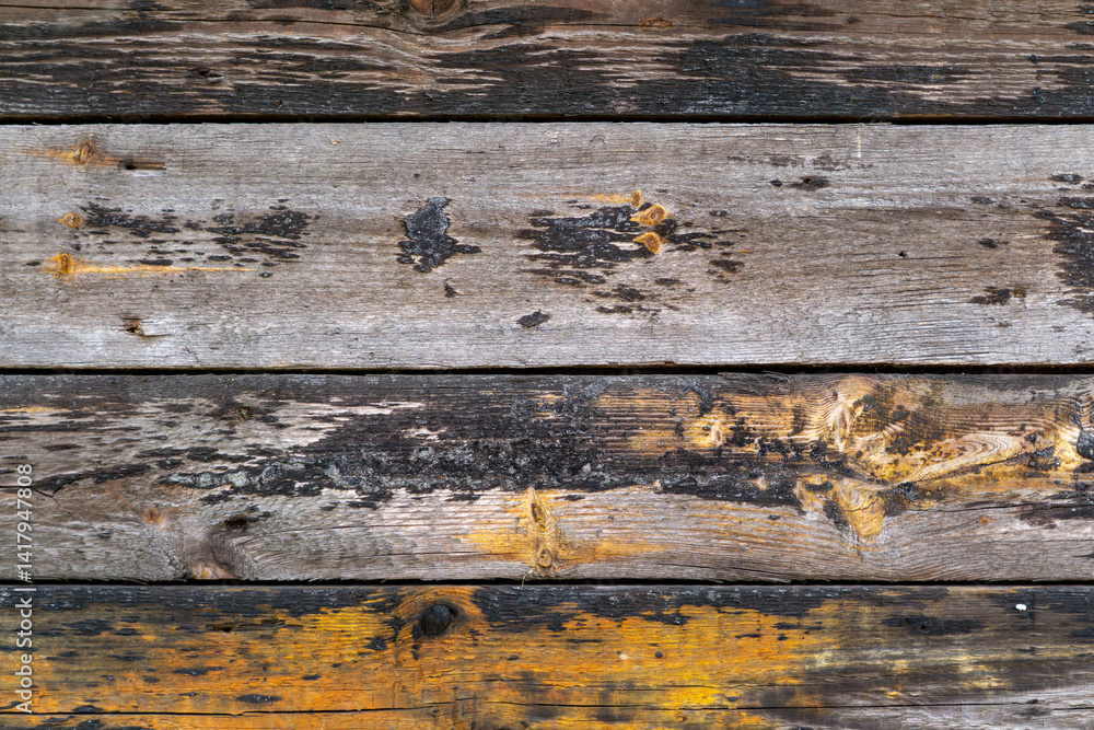 Fototapeta premium The photo shows old, damaged wooden boards with visible signs of wear, discoloration and yellow paint stains. The wood texture and color contrast give the photo a rustic, raw character