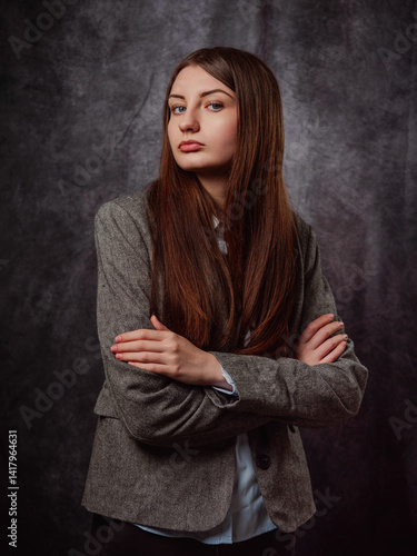 A young business woman is wearing a gray jacket and black pants. The model has long brown hair is elegant and is standing in front of a gray color background. Lady boss concept. Classic portrait.