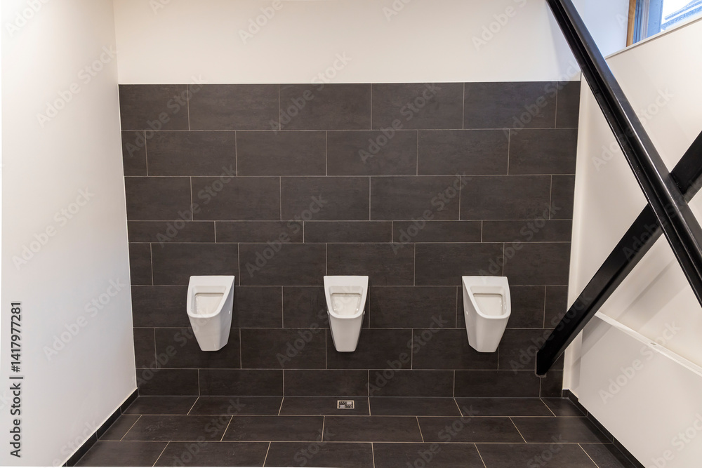 Row of white urinals in modern public restroom with dark tiles