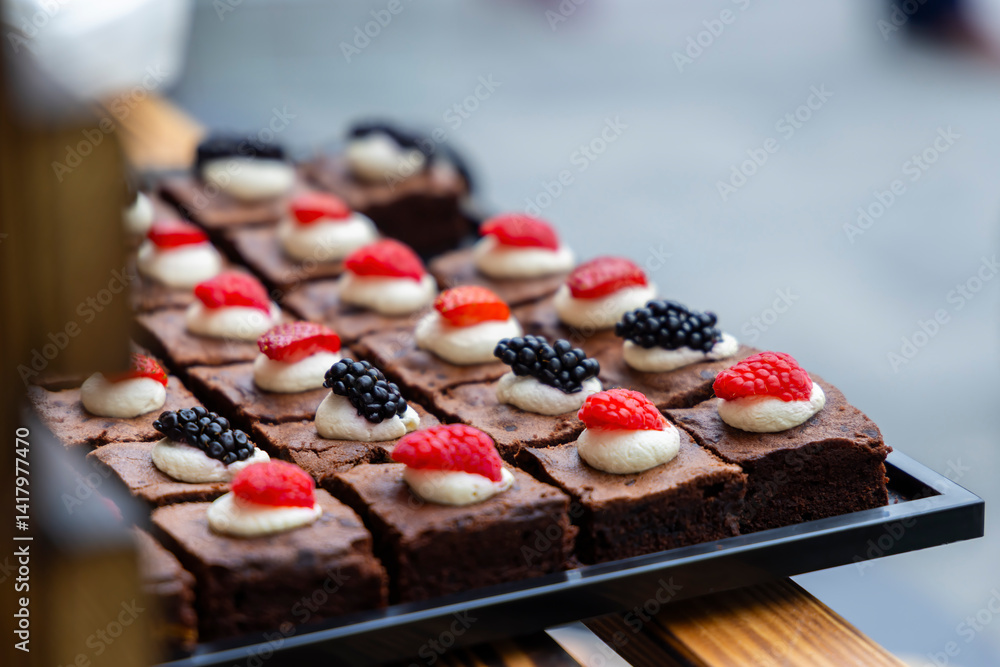 Catering service offering small brownies decorated with cream and berries
