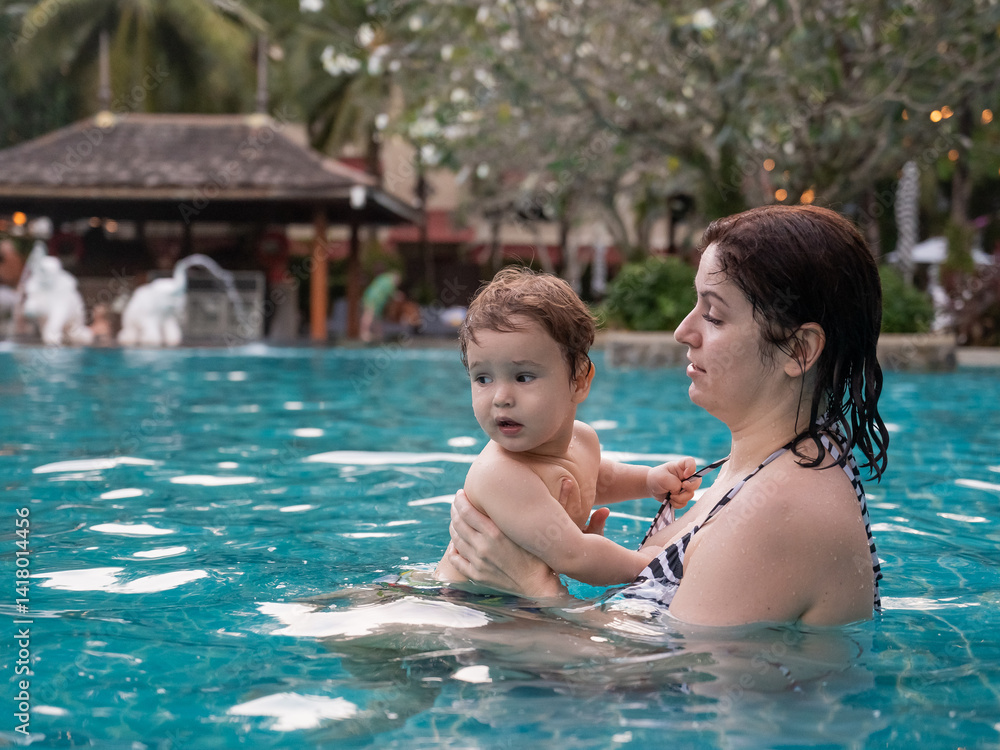 Caucasian woman holds son while swimming in pool on vacation. Caucasian woman holds son while swimming in pool on vacation.