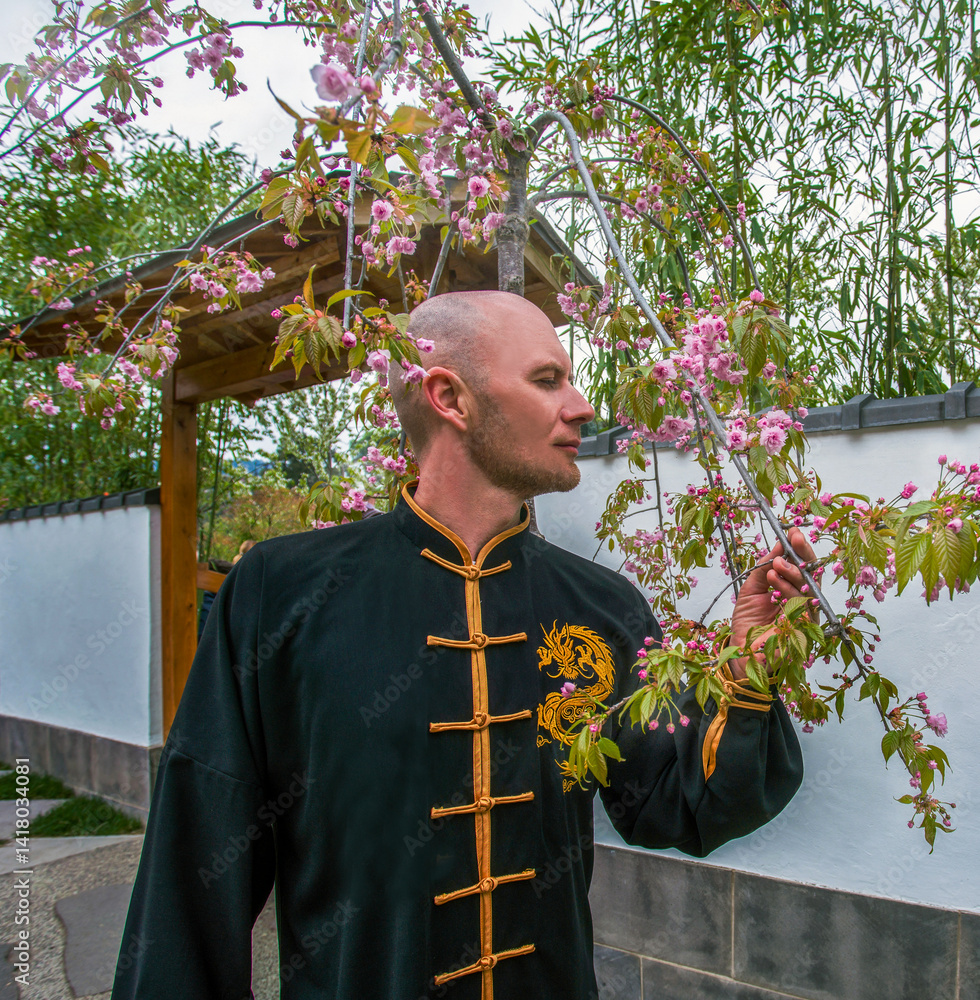 European man in Chinese buddhist suit near blossoming cherry trees