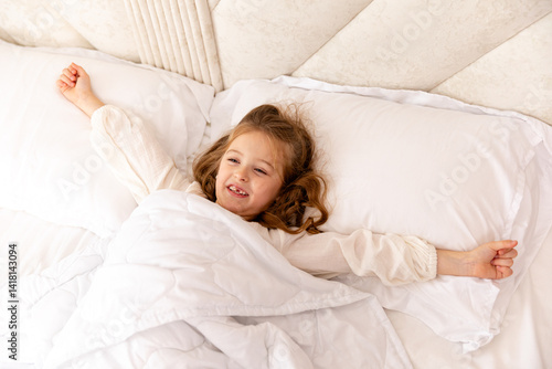 Cheerful little blonde girl in bed. Child woke up in bed with a good mood in the morning. textiles for the nursery. Have a nice day. Motherhood and childcare concept. High quality photo