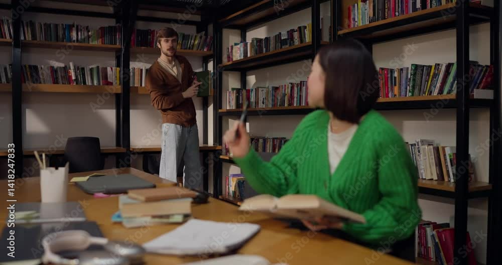 A brunette girl chooses a book from those offered to her by a guy in the library A brunette girl chooses a book from those offered to her by a guy in the library