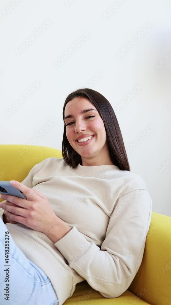 Young woman relaxing on yellow couch while using mobile phone at home Young woman relaxing on yellow couch while using mobile phone at home