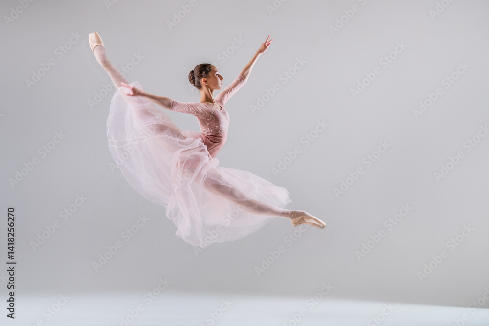 Ballerina soaring in a split jump in a pink tutu on neutral background. Ballerina soaring in a split jump in a pink tutu on neutral background.
