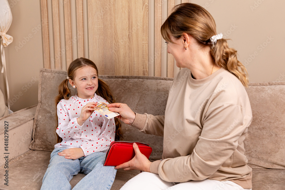 Pocket money. Mom gives child little girl cash money while they sitting on sofa in living room at home. Education, school and money saving concept. Junior savings account concept. High quality photo