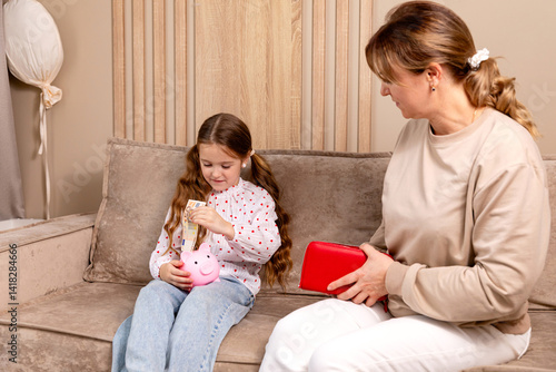 Obraz na płótnie Pocket money. Mom gives child little girl cash money while they sitting on sofa in living room at home. Education, school and money saving concept. Junior savings account concept. High quality photo w salonie