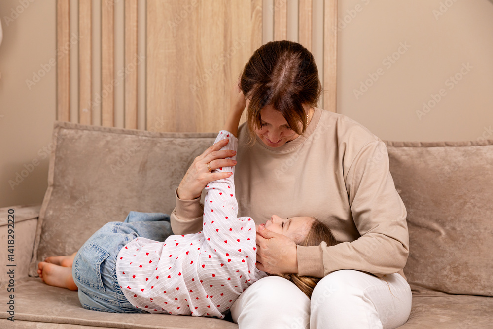 Cozy family moment. Little daughter resting on mom's lap in living room at home. Comfort, love, and family bonding concept. Child care and motherhood