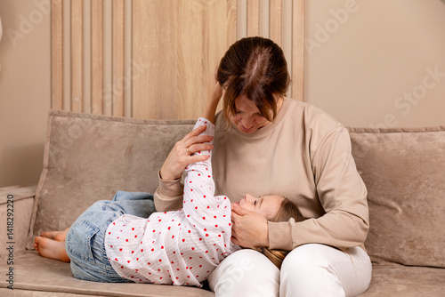 Cozy family moment. Little daughter resting on mom's lap in living room at home. Comfort, love, and family bonding concept. Child care and motherhood