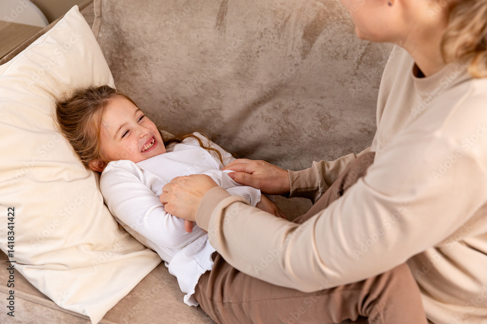 Close up hands of mom tickling kid daughter, laughing together on couch. Cheerful mother playing funny game with little cute girl at home, having fun, relaxing. Happy family. High quality photo