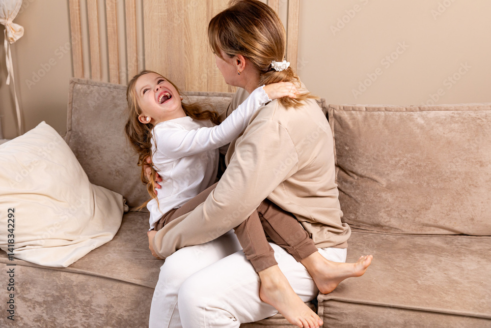 Happy mom tickling kid daughter, laughing together on couch. Cheerful mother playing funny game with little cute girl at home, having fun, relaxing. Happy family. High quality photo