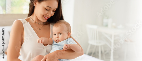 Beautiful young happy Asian mother hugging her cute little baby in bedroom at home