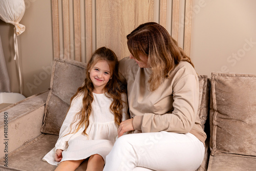 Cozy family moment. Little daughter resting on sofa with mom, hugging each other. Comfort, love, and family bonding concept. Child care and motherhood