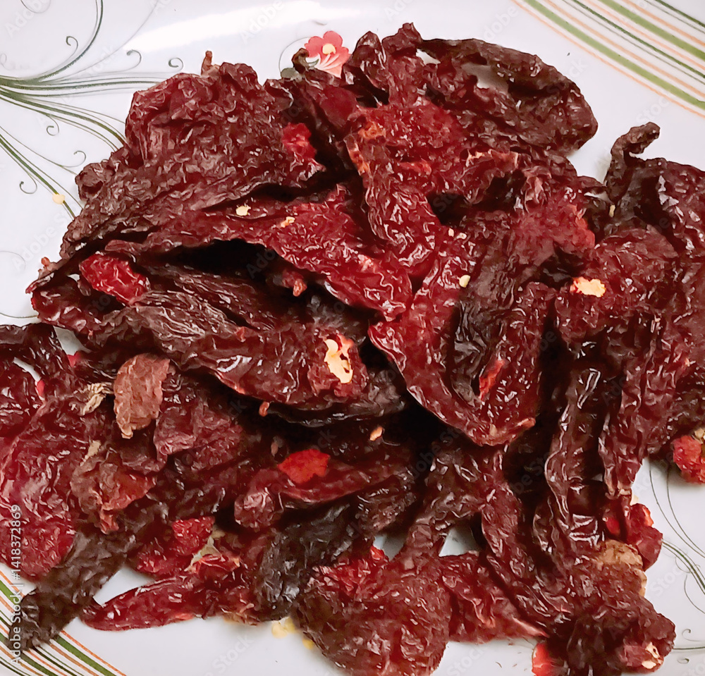 Obraz premium A vibrant pile of Kashmiri dry red chilies with deep red color and wrinkled texture, served on a patterned plate. Known for mild heat and rich color in Indian curries and spice blends.