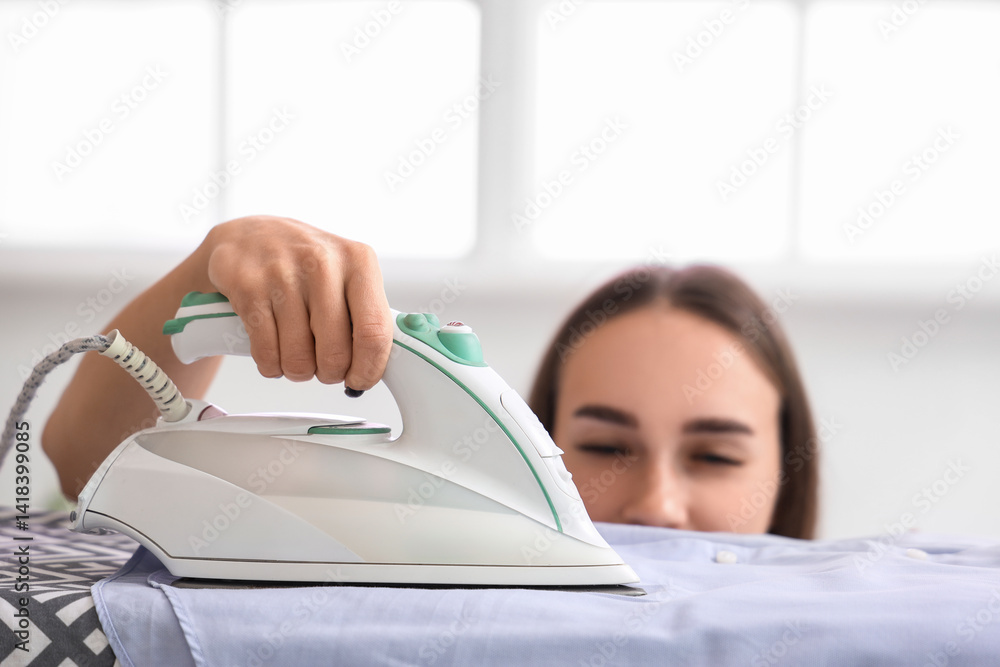 Pretty young woman ironing clothes at home, closeup