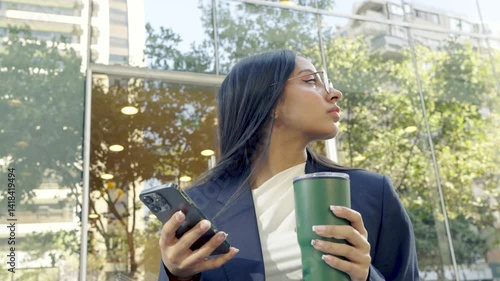 Native American woman with Hispanic features and Chilean descent, drinking from a mug and checking her phone in a business environment with a glass building in the background