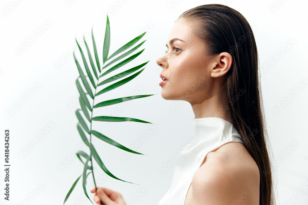 Elegant woman holding a green palm leaf, showcasing beauty and nature in a minimalistic studio setting.