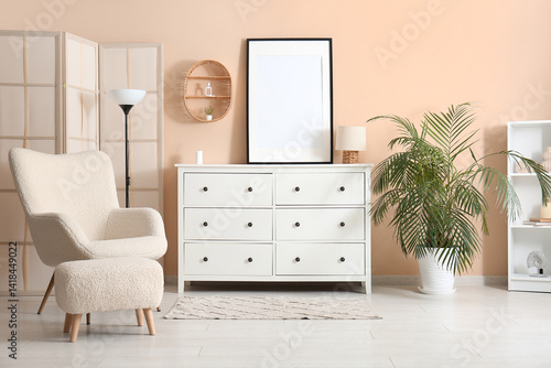 White chest of drawers with blank photo frame and comfortable armchair in room