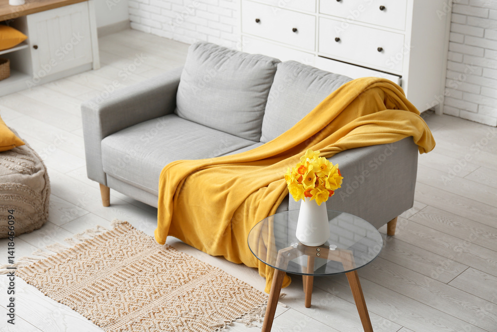 Cozy sofa with coffee table and narcissus flowers in living room