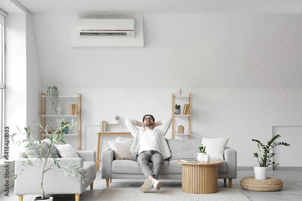 Fototapeta premium Young man resting on sofa with air conditioner in living room