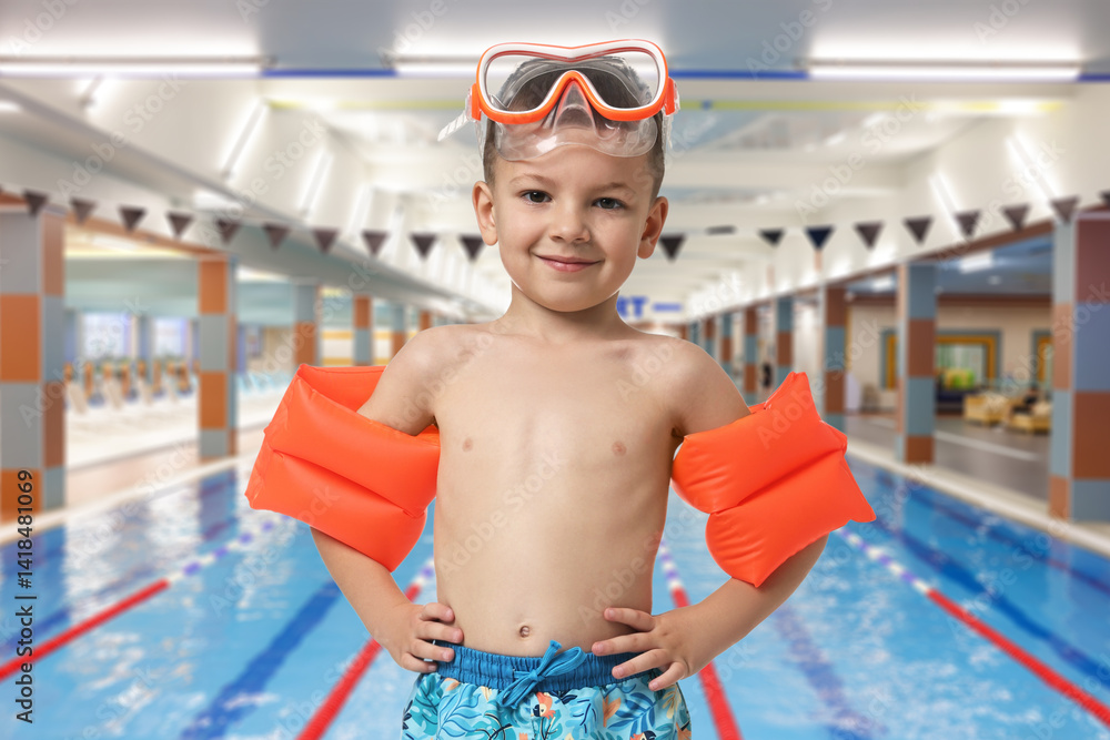 Cute little boy in trunks with diving mask and swim armbands at indoor swimming pool