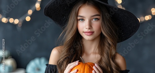 Obraz na płótnie A beautiful witch with long hair in a black dress and hat, holding a Halloween pumpkin. w salonie
