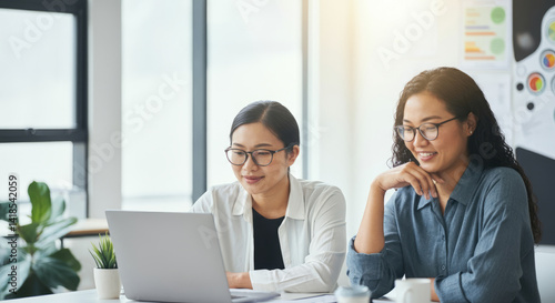 Asian female colleagues collaborating at office desk with laptop and documents