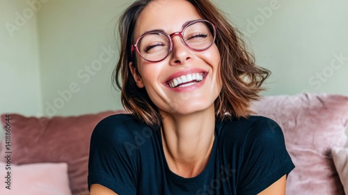 A beautiful woman with glasses is smiling widely, showcasing perfect teeth and radiating joy. The photo captures a moment of happiness and positive energy indoors.