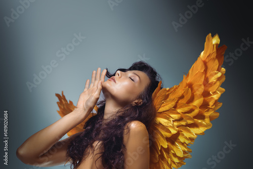 Foto Artistic beauty shot of a confident woman with radiant skin and golden wings, striking a sensual pose in studio light