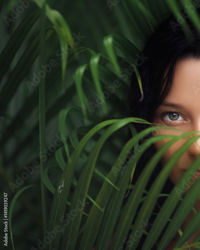 Obraz na płótnie A captivating close-up image featuring a woman eye, partially concealed by tropical leaves