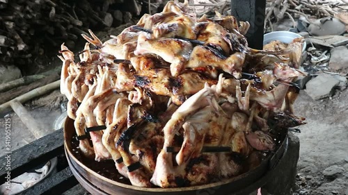 A pile of cooked grilled chicken is drained on a bamboo tray in a simple and traditional kitchen. It looks very delicious and tempting.
