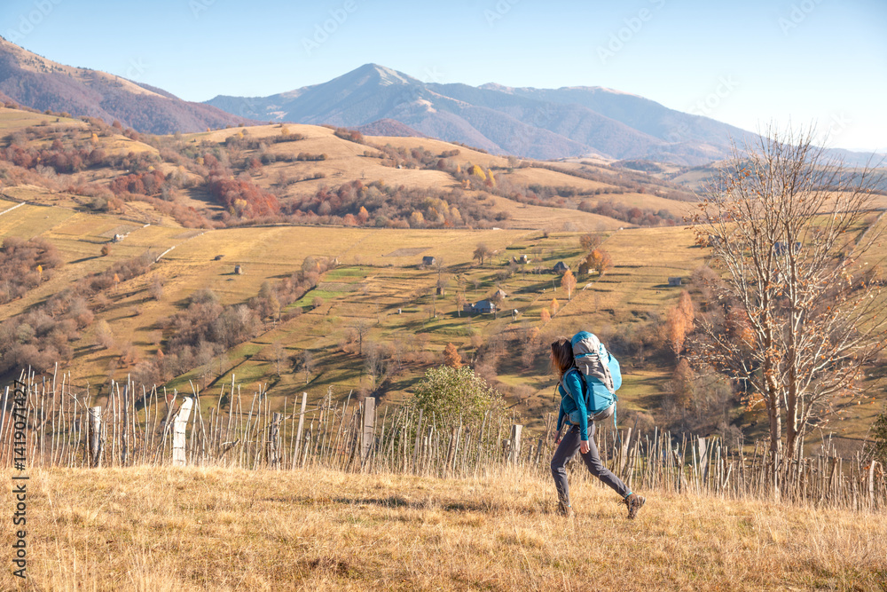 Woman backpacking in open mountain landscape during fall season, surrounded by panoramic alpine scenery Woman backpacking in open mountain landscape during fall season, surrounded by panoramic alpine scenery