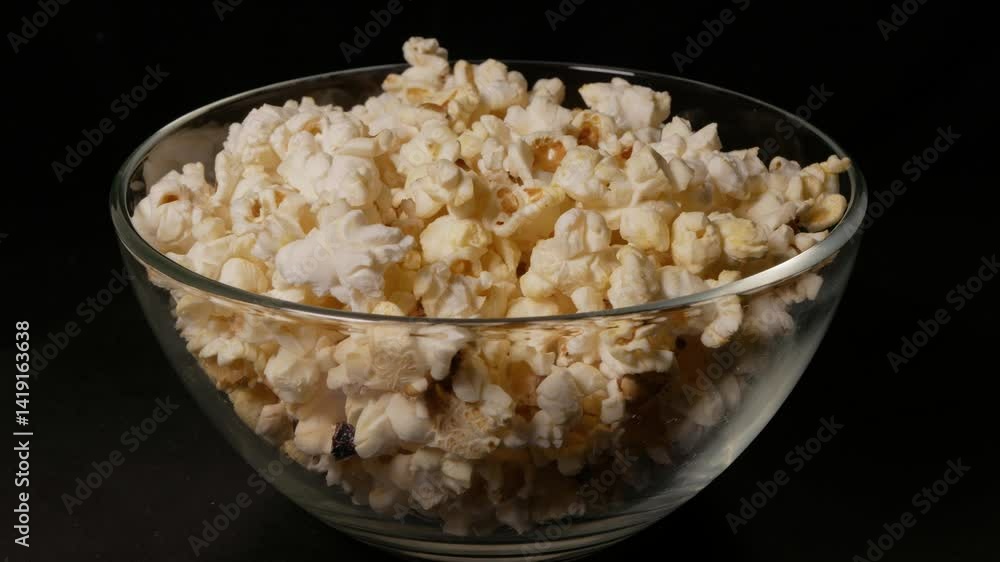 Popcorn in a glass bowl rotates on a black background. Close-up. Popcorn in a glass bowl rotates on a black background. Close-up.