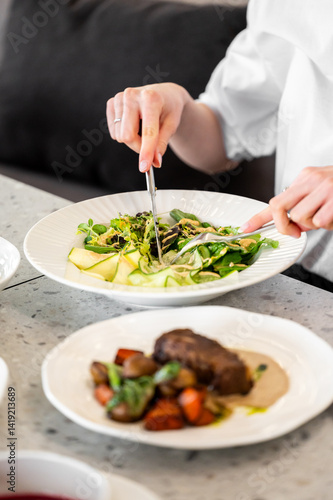 Wallpaper Mural A person is delicately cutting a fresh salad with greens and sliced cucumber, while a gourmet meat dish sits nearby. The stylish dining setup enhances the inviting atmosphere. Torontodigital.ca