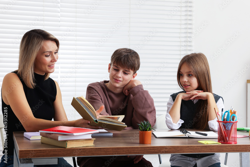 Smiling mother helping her children with homework at table indoors Smiling mother helping her children with homework at table indoors