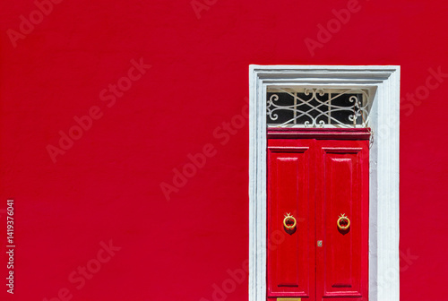 Obraz na płótnie Minimalist architectural photography. Red wall of residential building facade with red door in white wooden frame w salonie