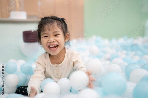 Joyful girl laughing in ball pit at indoor playground