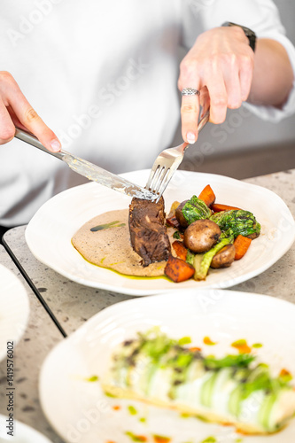 Wallpaper Mural A person is using a knife and fork to cut into a tender piece of meat with a creamy sauce, accompanied by roasted vegetables. The elegant dining setting creates an inviting atmosphere Torontodigital.ca