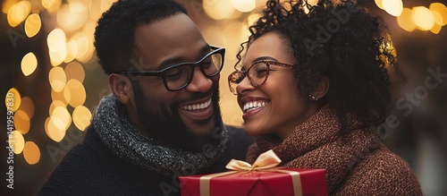 Couple exchanging Christmas gift, city lights background, possible use holiday card, social media