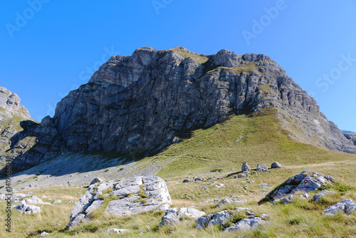 Majestic rocky peak under a clear blue sky, with green slopes and scattered boulders in Montenegro