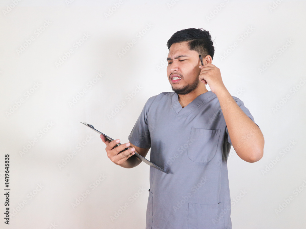 Asian male nurse shows shocked expression when he sees the note in clipboard he is holding Asian male nurse shows shocked expression when he sees the note in clipboard he is holding